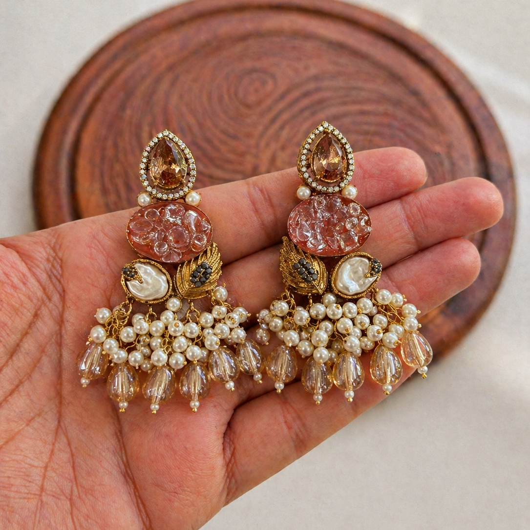 Ornate earrings held in a hand with a wooden coaster in the background