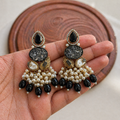 Decorative earrings held in a hand with a wooden coaster in the background
