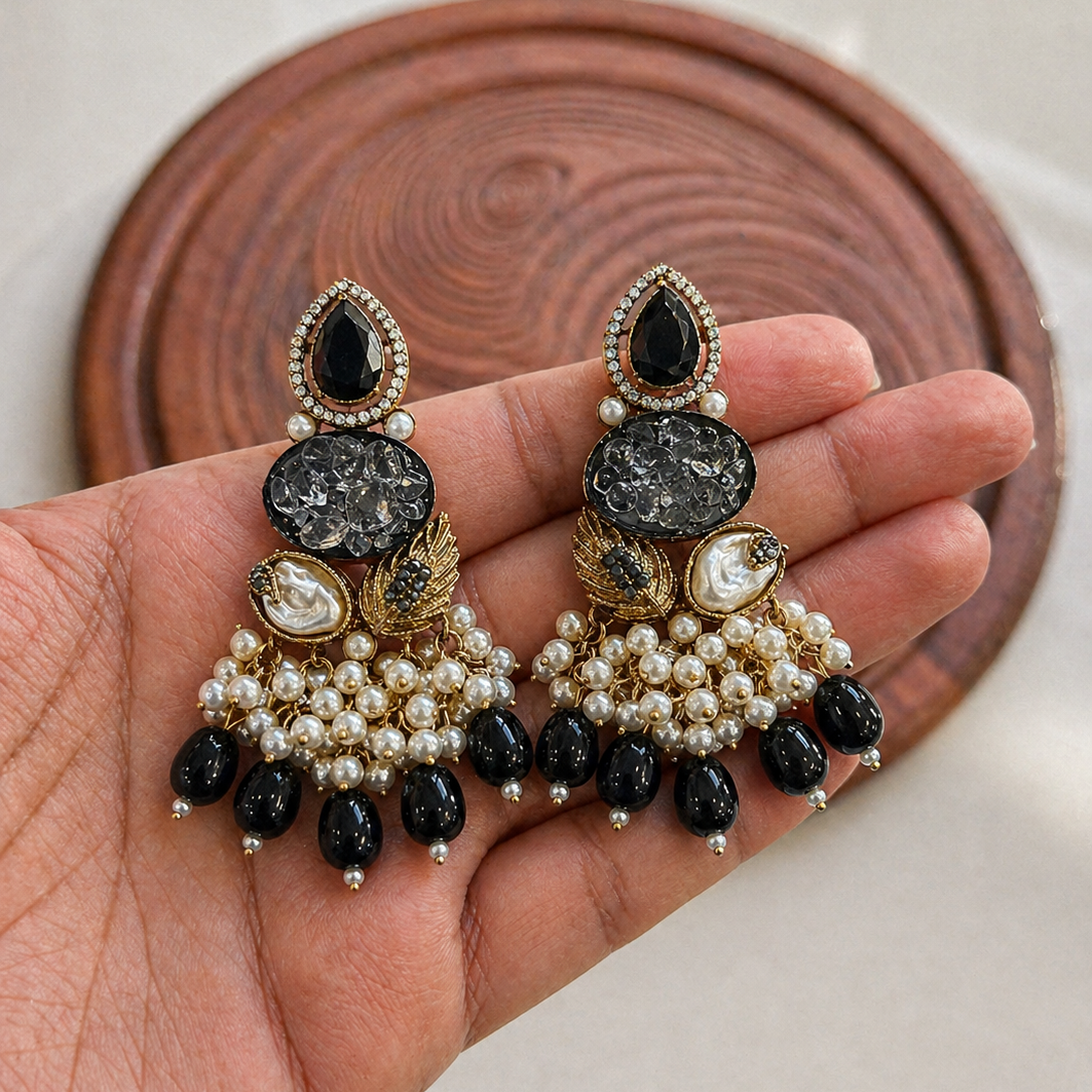 Decorative earrings held in a hand with a wooden coaster in the background