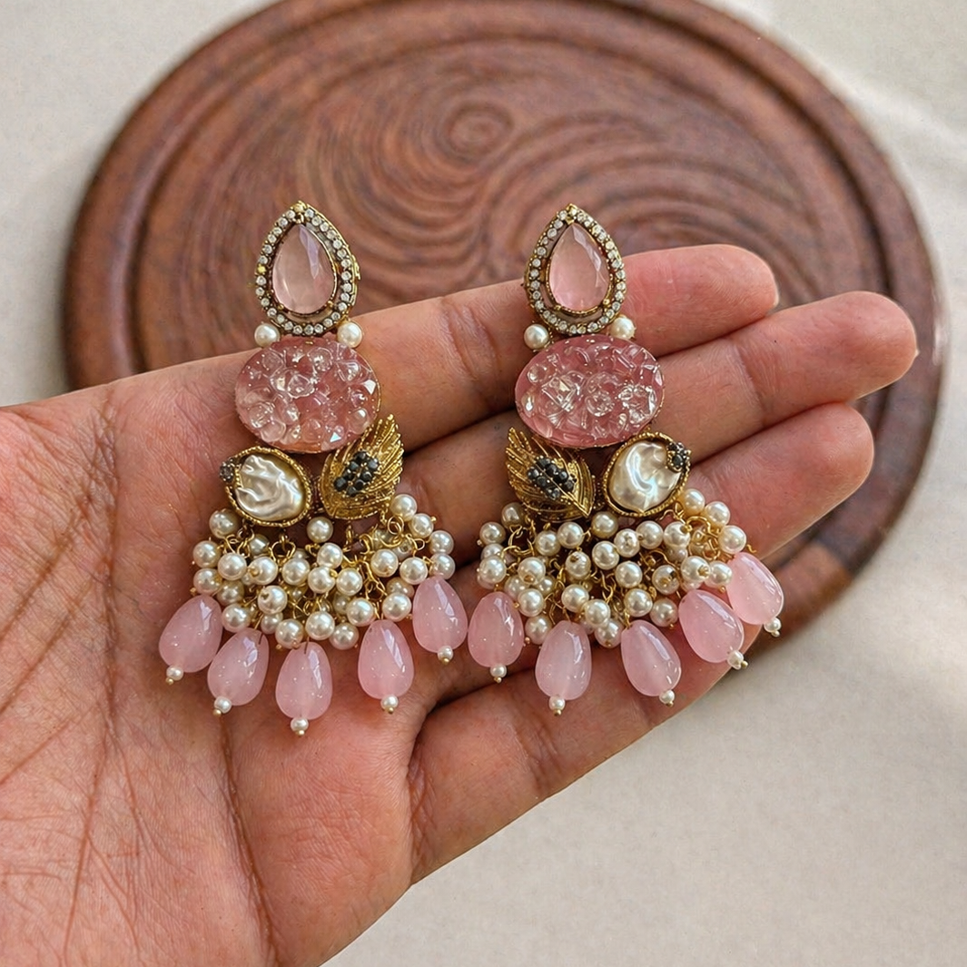 Pink and gold earrings held in a hand with a wooden background